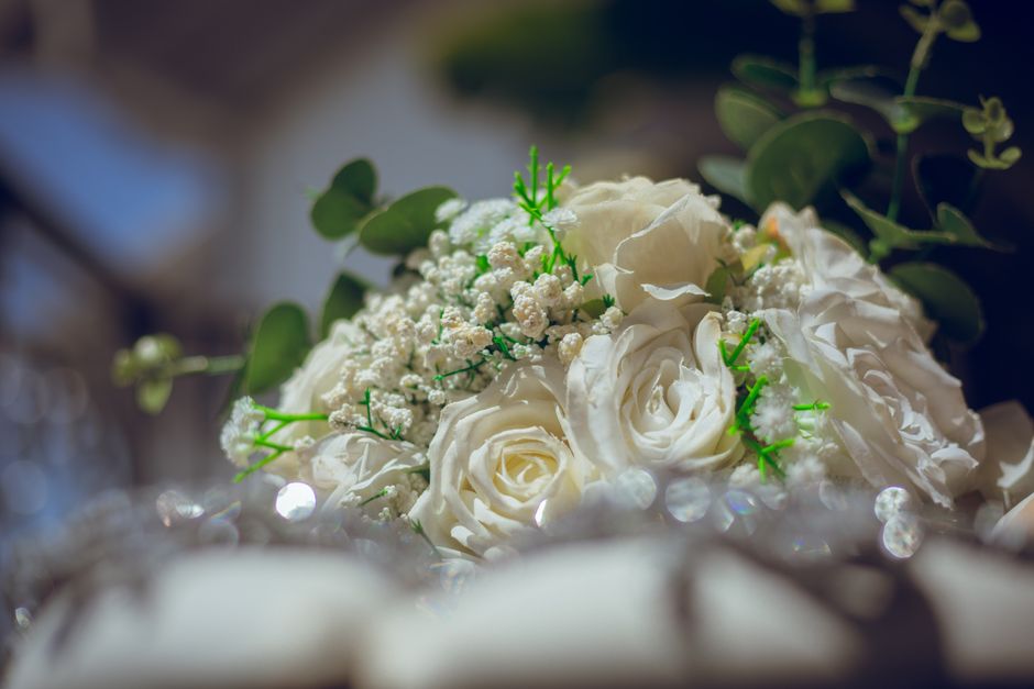A close-up image of a floral arrangement featuring predominantly white roses with delicate, softly curled petals, complemented by small white baby's breath flowers and green foliage with rounded eucal