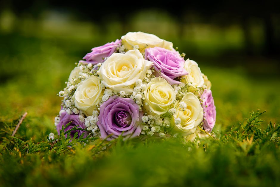 A close-up view of a floral bouquet arrangement featuring predominantly cream and light purple roses, accented with delicate white baby's breath flowers. The roses have lush, velvety petals with some 